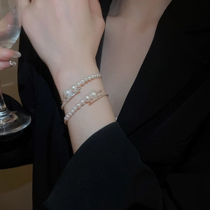 Detail of layered pearl bracelet with rhinestones worn on wrist against black blazer