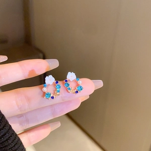 Detailed view of floral stud earrings with blue crystals and pearls held by hand
