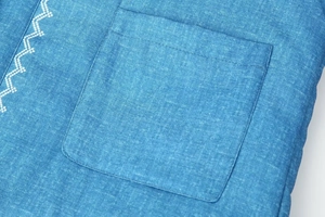 Detail der blauen Denim-Baumwolljacke mit weißer Wellenstickerei und quadratischer Tasche