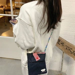 Detail of blue denim crossbody bag with red checkered flap and colorful beaded strap