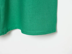 Close-up of vibrant green linen blend fabric texture and stitching detail on dress hem