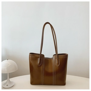 Detail of brown leather tote bag with white stitching on a minimalist table