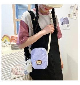 Detail of light purple corduroy crossbody bag with brown bear patch and white plush charm