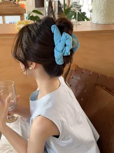 Detail of light blue pleated fabric hair claw clip worn on a low bun in a cafe setting