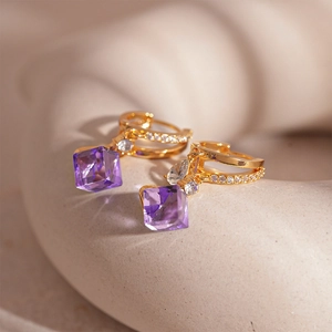 Dettaglio orecchini a cerchio dorati con pavé di zirconi e ciondoli a cristallo viola quadrati