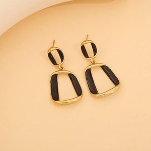 Macro detail of geometric gold finish earrings with black drip oil enamel texture