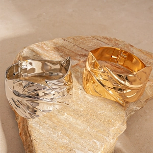 Golden and silver leaf-shaped open cuffs with metallic wrinkle textures on stone