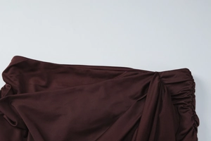 Detail showing the elegant ruched draping and pleated texture of the dark brown skirt
