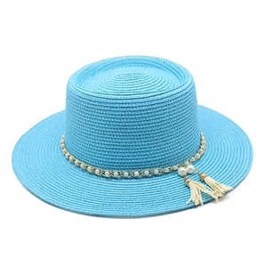 Détail d'un chapeau de paille bleu ciel avec chaîne dorée, perles et glands blancs