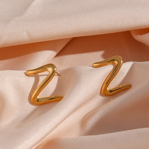 Detailed view of gold Z-shaped stud earrings on elegant pink silk background