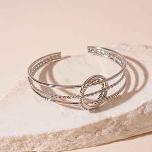 Detail view of silver triple-layer geometric cuff bracelet on a white textured stone