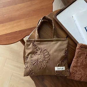 Close-up of camel suede floral embroidery and simple wish label on handheld bag