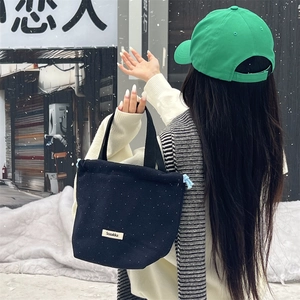 Outdoor shot of a black polka dot drawstring canvas tote bag with woven brand label