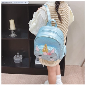 Toddler girl wearing light blue unicorn backpack with sequins in home setting