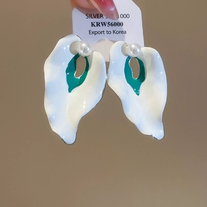 Close-up of artistic calla lily earrings with white enamel, green center and pearl accent