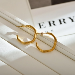 Minimalist gold-plated irregular wavy earrings on a textured white leather stand