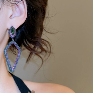 Vue rapprochée de boucles d'oreilles losanges avec cristaux violets et gemme verte sur l'oreille