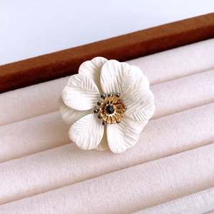 Detailed close-up of white floral ring with gold center on a beige velvet background
