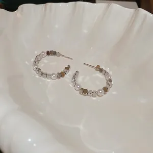 Elegant C-shaped silver earrings with white pearls and square beads on a shell dish
