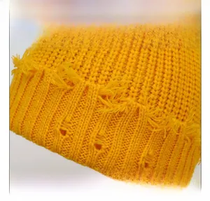 Détail du bonnet en maille jaune montrant la texture épaisse et les trous effilochés