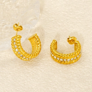 Close-up of golden twisted hoop earrings with sparkling rhinestones and woven texture