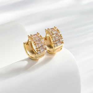 Elegant gold huggie earrings with cubic zirconia stones on a white geometric pedestal