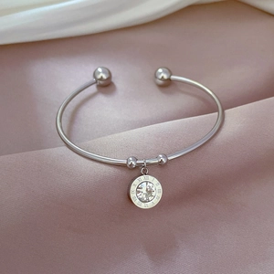 Detailed shot of silver steel bangle with Roman numeral charm and single crystal