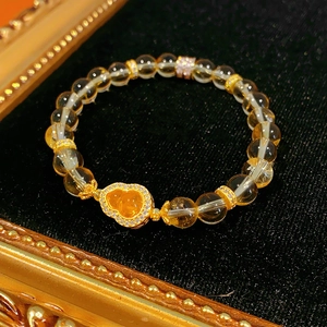 Détail d'un bracelet en perles de citrine avec un pendentif gourde dorée sur velours