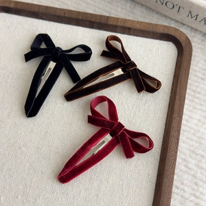 Three velvet bow hair clips in black, brown, and wine red on a wooden jewelry tray