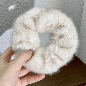 Close-up of a soft plush cream-white hair scrunchie held in hand with fluffy texture
