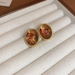 Close-up of amber resin oval stud earrings with textured gold-tone metal borders