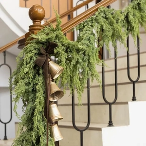 Artificial cypress garland with gold bells and brown velvet bow on wooden stairs