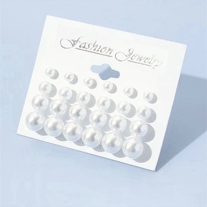 Detailed view of 12 pairs of minimalist pearl stud earrings on white jewelry card