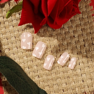Short square pink press-on nails with white heart patterns on a floral background