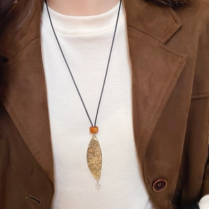 Close-up of golden leaf pendant with orange bead on a long black cord necklace