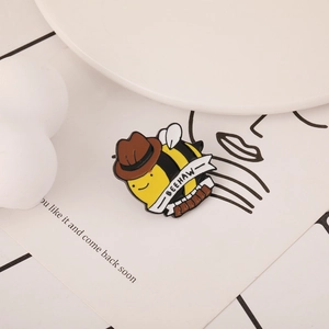 Detail of a cartoon bee enamel pin with cowboy hat and Beehaw banner on card