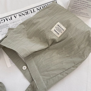 Close-up of sage green pleated canvas bag with vertical stitching and silver magnetic buckle