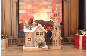 Detail of illuminated carbonized wood Christmas house and church tower with snow decor