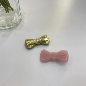 Detail of pink and green resin bow hair clips with France Handmade text on white desk