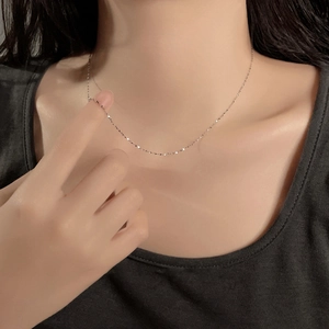 Detail of thin silver stainless steel chain necklace worn on a woman's collarbone