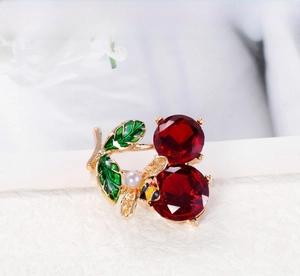 Detail of cherry brooch with red crystals, green enamel leaves and a small pearl bee