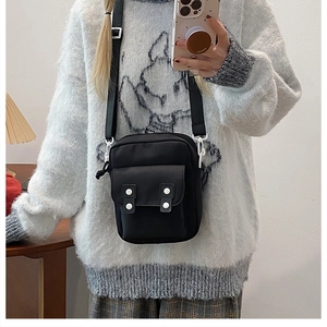Detail of black nylon crossbody phone bag with white buckles and adjustable shoulder strap