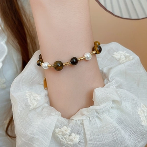 Detail view of pearl and tiger eye beaded bracelet on wrist with elegant lace sleeve