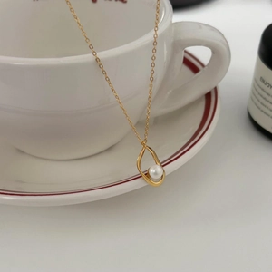 Irregular golden hollow pendant necklace with a pearl hanging on a white ceramic cup