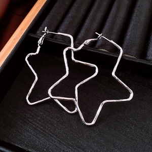 Macro detail of large silver star-shaped hoop earrings on black velvet jewelry display