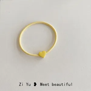 Dettaglio macro di un elastico per capelli giallo con ciondolo a cuore opaco