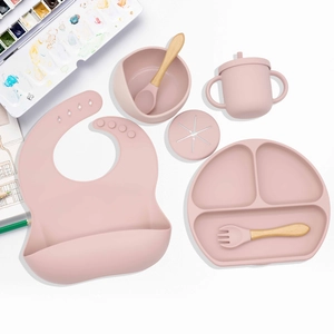 Pink silicone baby feeding set with suction bowl, bib and dinner plate on white table