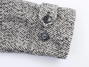 Close-up of herringbone wool coat cuffs with black buttons and detailed fabric texture