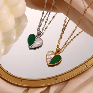 Minimalist heart pendant necklace with green and white shell inlay on a golden mirror