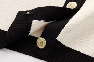 Detail of knit cardigan with golden crest buttons and black contrast ribbed edges
